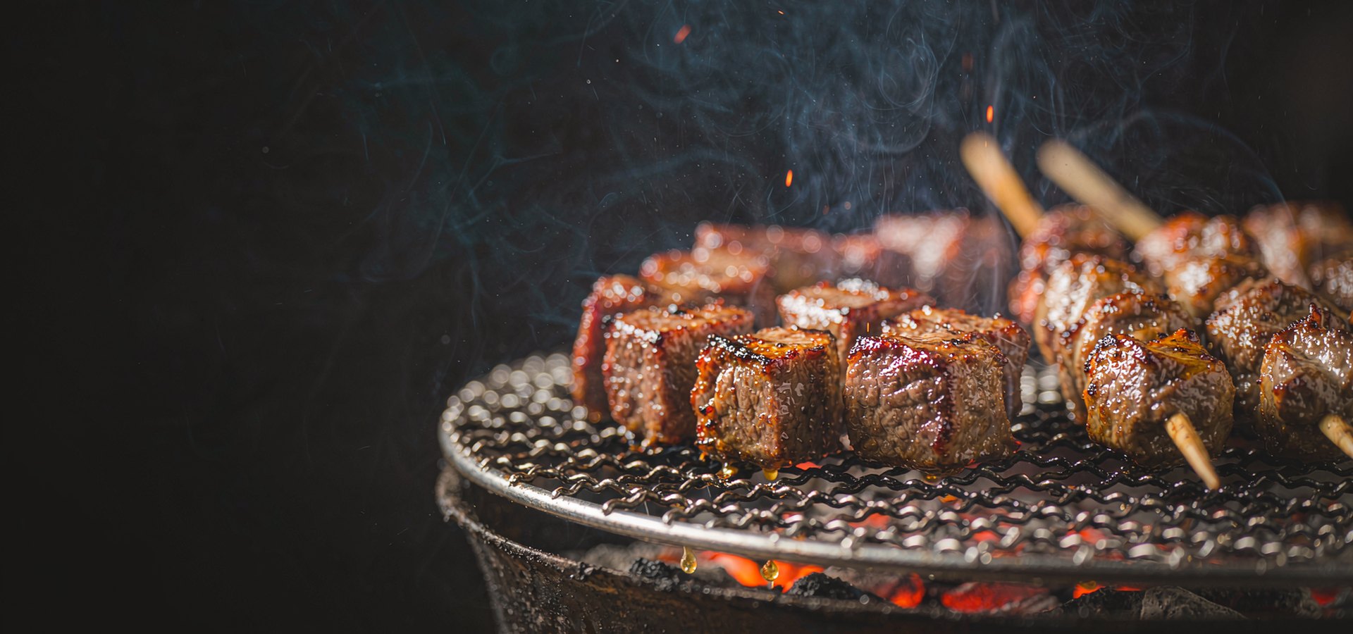 炭火烤网上并排炙烤的牛肉块与羊肉串，表面焦黄油亮，青烟上升，暗色背景