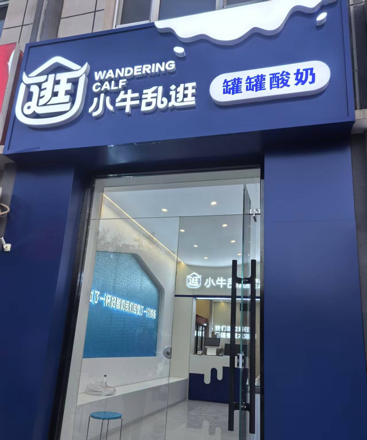 蓝底的招牌上，左边是“小牛乱逛”，右边是“罐罐酸奶”。